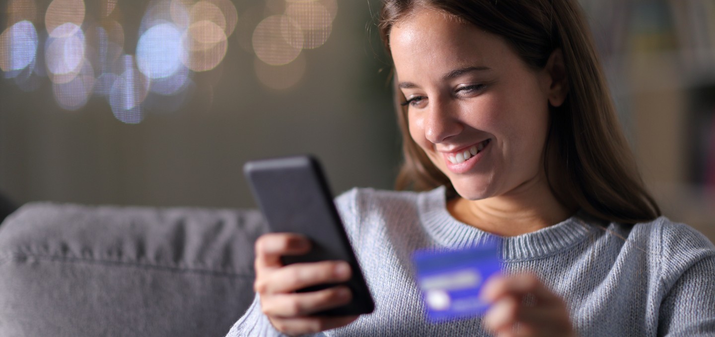 a woman viewing her mobile device holding a debit/credit card