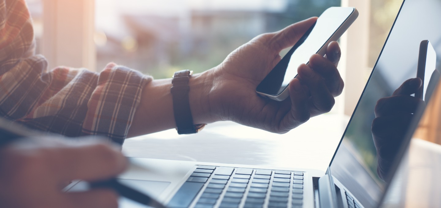 a person holding their mobile phone and working on their laptop