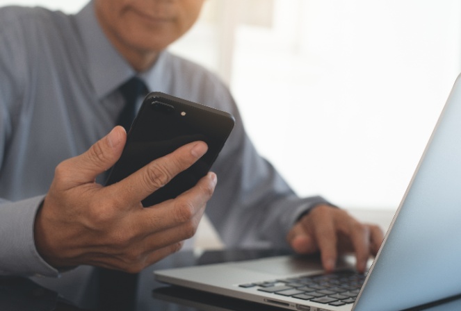 a man viewing his cell phone and working on his laptop