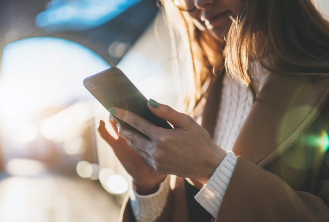 A woman wearing a sweater and jacket scrolling on her phone.